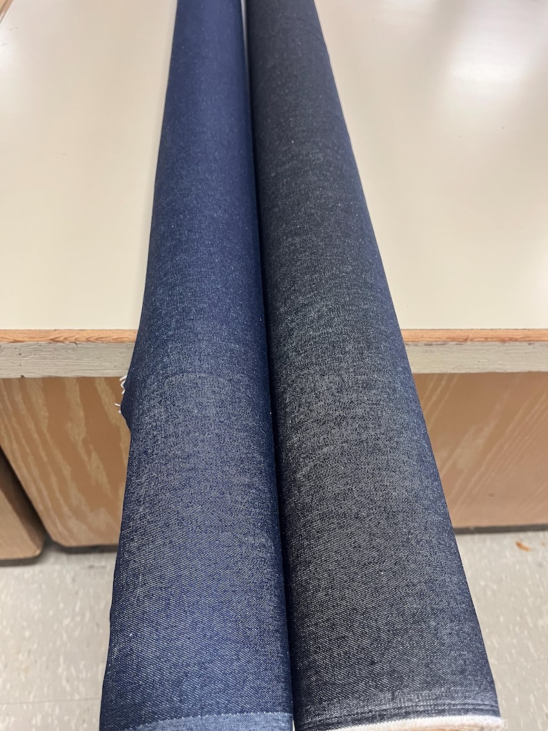 May include: Two rolls of dark blue denim fabric. The fabric on the left is a lighter shade of blue than the fabric on the right.
