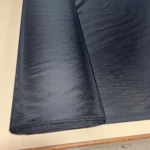 May include: A roll of black sheer fabric, folded and lying on a light brown surface.