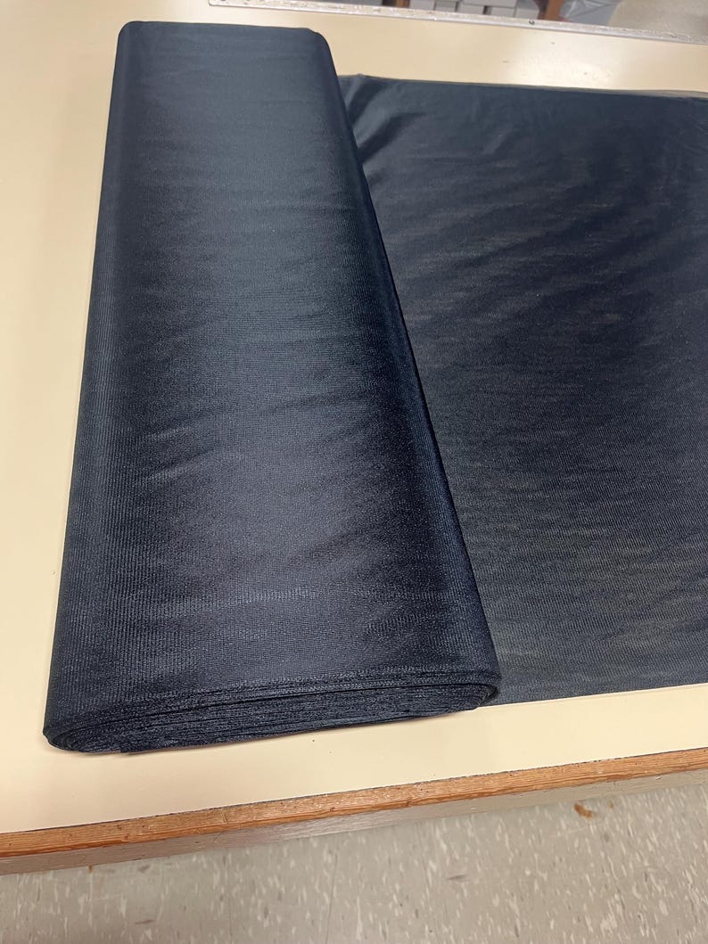May include: A roll of black sheer fabric, folded and lying on a light brown surface.