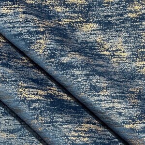 May include: A close-up of a blue fabric with a metallic gold shimmer. The fabric has a textured, brushed look and a subtle sheen.