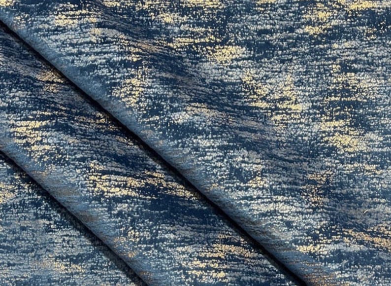 May include: A close-up of a blue fabric with a metallic gold shimmer. The fabric has a textured, brushed look and a subtle sheen.
