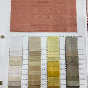 May include: A fabric swatch book featuring a large, textured, reddish-brown fabric sample at the top. Below are rows of smaller fabric swatches in various neutral and earth-tone colors, labeled with codes like SD-001 and SD-014.