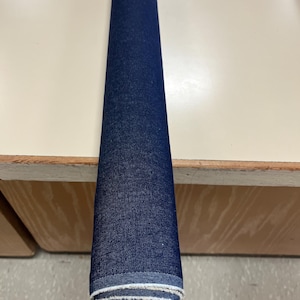 May include: A roll of dark blue denim fabric with white stitching around the edges.