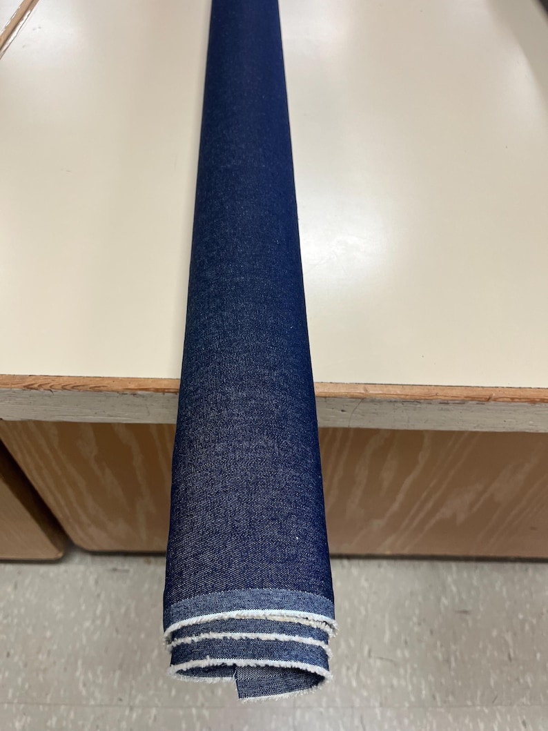 May include: A roll of dark blue denim fabric with white stitching around the edges.