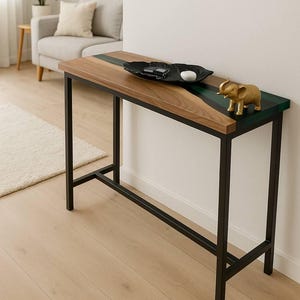 Op de afbeelding: Een moderne consoletafel met een houten blad en zwarte metalen poten. Het tafelblad heeft een donkergroene en zwarte harsinleg. Een gouden olifantenbeeldje en een zwarte decoratieve kom staan op de tafel.