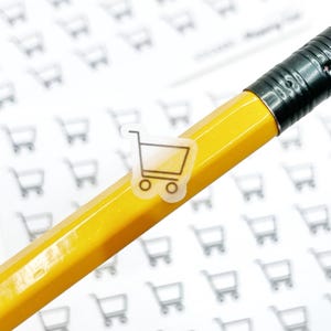 May include: A yellow pencil with a red eraser tip, with a small clear sticker of a shopping cart on the side. The background is covered with small shopping cart graphics.