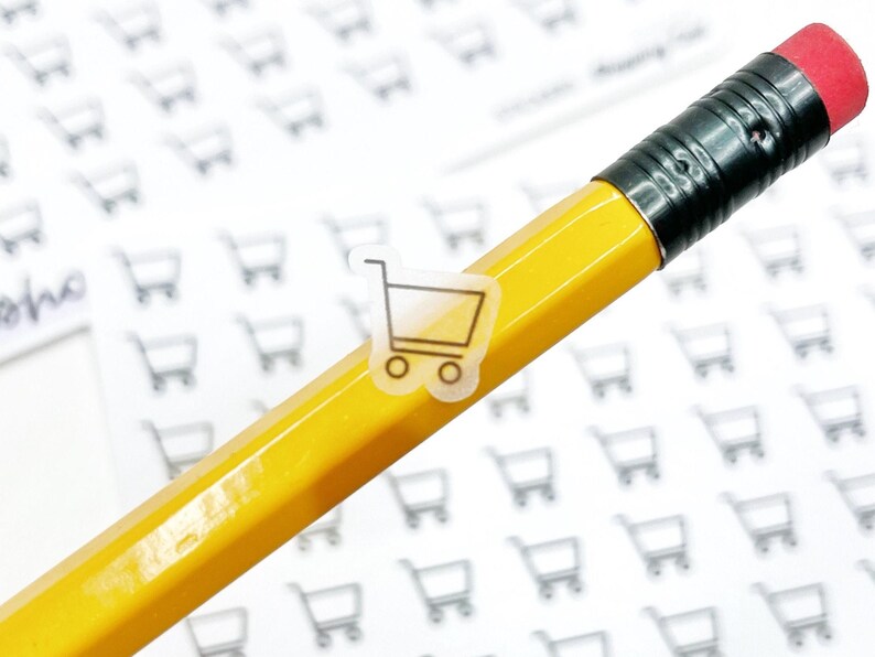 May include: A yellow pencil with a red eraser tip, with a small clear sticker of a shopping cart on the side. The background is covered with small shopping cart graphics.