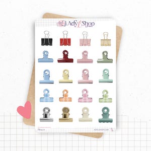 May include: A sticker sheet featuring twenty individual illustrations of binder clips in various colors and patterns, including solid black, red, pink, gold, blue, green, and plaid designs. The top of the sheet displays the text Adyl Shop.
