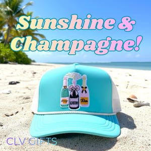 Peut inclure: Casquette de camionneur turquoise avec un dos en filet blanc, ornée d'un motif brodé de bouteilles de champagne. La casquette porte les inscriptions "Sunshine & Champagne!" et "CLV GIFTS". La casquette est sur une plage de sable avec des palmiers et un ciel bleu en arrière-plan.