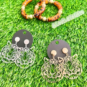 May include: A pair of gold tiger head earrings with a black background. The earrings are on a black card with a gold stud.