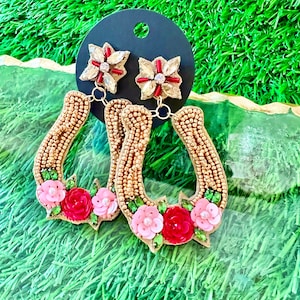 May include: A pair of gold horseshoe-shaped earrings with pink and red flower embellishments. The earrings are beaded and have a dangling flower charm.