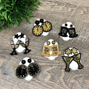 May include: Six pairs of beaded earrings with a New Year's Eve theme. The earrings feature gold and black beads and include designs such as champagne glasses, clocks, and party hats with the words "Happy New Year" and "New Year".