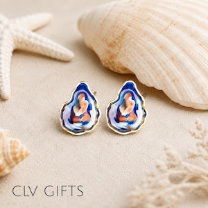 May include: A pair of stud earrings shaped like oyster shells, featuring an abstract enamel design in shades of deep blue, light purple, and peach, outlined with a thin gold-tone metal border. The text CLV GIFTS is visible at the bottom.