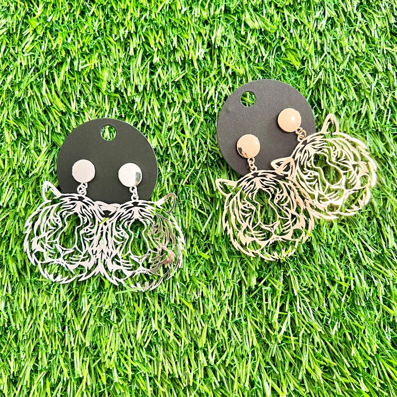 May include: Two pairs of earrings featuring a tiger face design. One pair is silver and the other is gold.