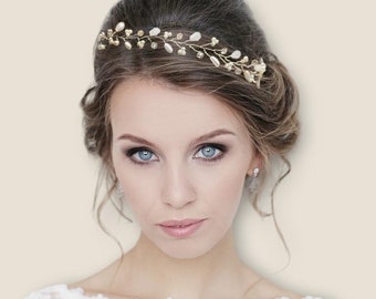May include: A bride with a simple updo hairstyle wears a delicate gold and white beaded hairpiece. The hairpiece is a vine-like design with small pearls and gold accents.