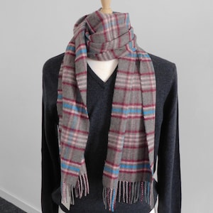 Peut inclure: Une écharpe à carreaux gris, rose et bleu avec des franges aux extrémités.
