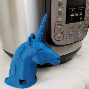 May include: A blue 3D printed unicorn head with a horn, used as a handle for an Instant Pot pressure cooker. The Instant Pot has a digital display and buttons for various cooking functions, including Soup/Broth, Meat/Stew, Bean/Chili, Poultry, Slow Cook, Sauté, Pressure Level, Keep Warm, Delay Start, and Cancel.
