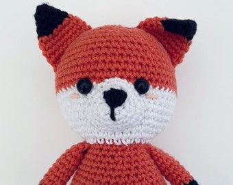 May include: A crocheted fox plush toy with orange fur, white face, and black ears, nose, and feet.