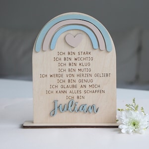 May include: Wooden sign with a rainbow design and a heart in the center. The sign has the text "ICH BIN STARK, ICH BIN WICHTIG, ICH BIN KLUG, ICH BIN MUTIG, ICH WERDE VON HERZEN GELIEBT, ICH BIN GENUG, ICH GLAUBE AN MICH, ICH KANN ALLES SCHAFFEN, ICH BIN Julian" in brown lettering.