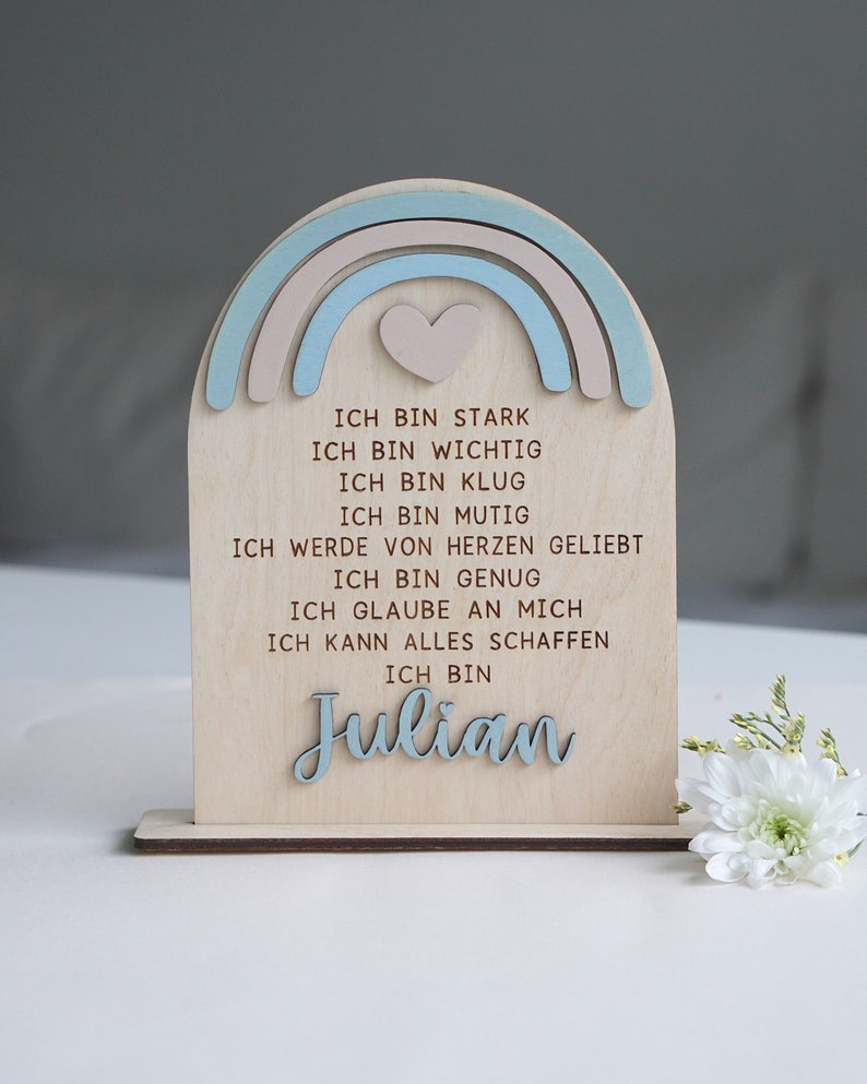 May include: Wooden sign with a rainbow design and a heart in the center. The sign has the text "ICH BIN STARK, ICH BIN WICHTIG, ICH BIN KLUG, ICH BIN MUTIG, ICH WERDE VON HERZEN GELIEBT, ICH BIN GENUG, ICH GLAUBE AN MICH, ICH KANN ALLES SCHAFFEN, ICH BIN Julian" in brown lettering.