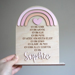 May include: A wooden rainbow with a pink heart and the text "ICH BIN STARK, ICH BIN WICHTIG, ICH BIN KLUG, ICH BIN MUTIG, ICH WERDE VON HERZEN GELIEBT, ICH BIN GENUG, ICH GLAUBE AN MICH, ICH KANN ALLES SCHAFFEN, ICH BIN Sophie"