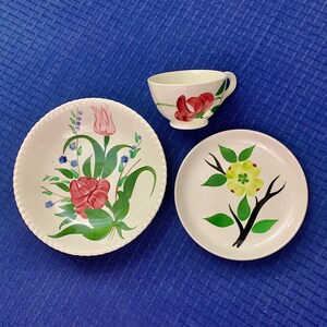 May include: Three vintage ceramic plates with floral designs. The plates feature a pink and green floral design, a yellow and green floral design, and a red and green floral design. The plates are white with a scalloped edge.