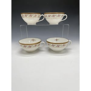 May include: Four white teacups with a floral design and gold trim. The cups are arranged in two rows of two, with a clear shelf in the middle. The floral pattern includes pink flowers and green leaves.