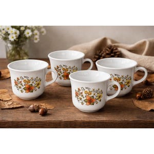 May include: Four white ceramic mugs with a floral design in shades of orange, yellow, and green. The mugs have a rounded shape with a handle and are arranged on a wooden surface. The mugs are part of a set.