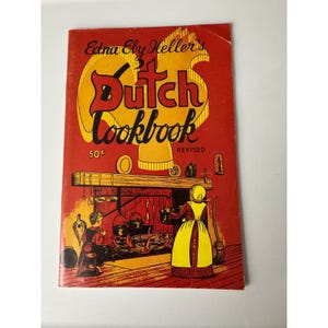 May include: A vintage cookbook titled "Dutch Cookbook" by Edna Ely Heller. The cover is red with yellow lettering and illustrations, including a Dutch kitchen scene. The price is listed as 50¢.