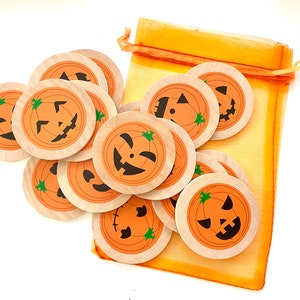 May include: A set of 10 wooden pumpkin face game pieces in a orange mesh bag. The pieces are round and have different jack-o-lantern faces.