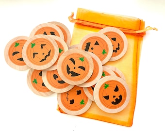 May include: A set of 10 wooden pumpkin face game pieces in an orange mesh bag. The pieces are round and have different jack-o-lantern faces.
