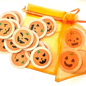 May include: A set of 12 wooden pumpkin-shaped Halloween decorations with different jack-o'-lantern faces. The decorations are in a small orange mesh bag.