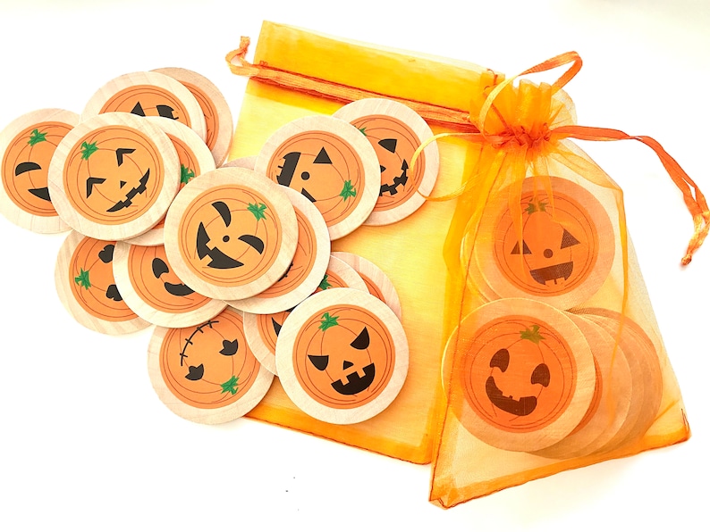 May include: A set of 12 wooden pumpkin-shaped Halloween decorations with different jack-o'-lantern faces. The decorations are in a small orange mesh bag.