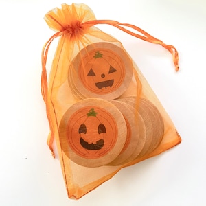 May include: A set of orange and brown wooden pumpkin-shaped ornaments with happy faces, packaged in a sheer orange organza bag.