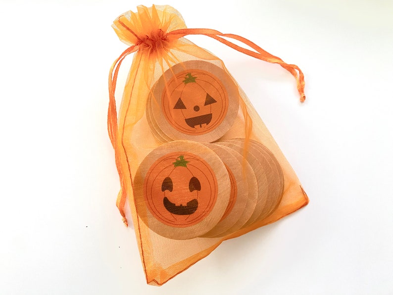 May include: A set of orange and brown wooden pumpkin-shaped ornaments with happy faces, packaged in a sheer orange organza bag.