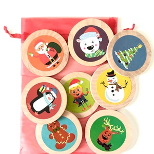 May include: A set of eight wooden Christmas ornaments with different festive designs, including Santa Claus, a penguin, a snowman, a gingerbread man, an elf, a reindeer, a polar bear, and a Christmas tree. The ornaments are in a red drawstring bag.