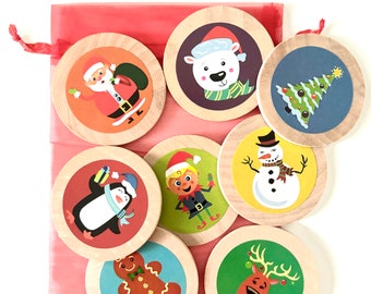 May include: A set of eight wooden Christmas ornaments with different festive designs, including Santa Claus, a penguin, a snowman, a gingerbread man, an elf, a reindeer, a polar bear, and a Christmas tree. The ornaments are in a red drawstring bag.
