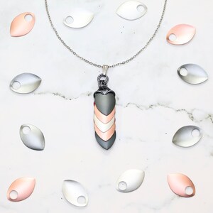 May include: A silver chain necklace with a pendant made of three overlapping scales in silver, copper, and rose gold. The pendant is shaped like a dragon scale. The image also shows several loose dragon scales in silver, copper, and rose gold.