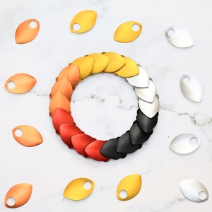 May include: A set of metal dragon scales in various colors, including red, orange, yellow, silver, and black. The scales are arranged in a circle, with the colors transitioning from red to black. The scales are also available individually, with a hole in each scale for attaching to a project.