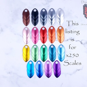 May include: A set of 250 metallic dragon scales in various colors, including brown, black, gray, silver, pink, red, orange, gold, green, blue, and purple. The scales are arranged in rows on a white marble surface. This listing is for 250 scales.