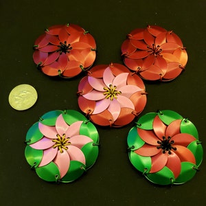 May include: Five decorative metal flowers in shades of red, pink, and green. The flowers are made of interlocking metal scales and have a spiral design.
