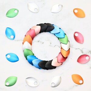 May include: A set of colorful metal scales for making a dragon scale mail bracelet. The scales are arranged in a circle, with the colors ranging from pink to blue. The scales are all the same size and shape, and they have a smooth, shiny finish.  "Show off your inner dragon" text is visible in the image.
