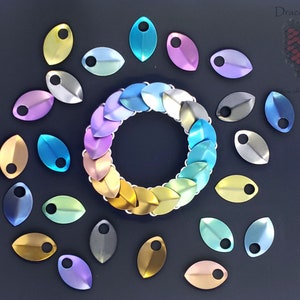 May include: A colorful metal bracelet made of individual scales, with additional scales in various colors scattered around it. The scales are in a rainbow pattern, with gold, yellow, green, blue, purple, and pink.