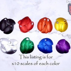May include: Ten sets of ten metal dragon scales in various colors, including black, red, silver, green, blue, and purple.  The scales are arranged in a circle on a white surface.  "This listing is for x10 scales of each color" is written below the scales.