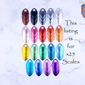 May include: Twenty-five metal dragon scales in various colors, including brown, black, silver, pink, red, orange, gold, green, blue, and purple. The scales are arranged in three rows on a white marble surface. The text "This listing is for x25 Scales" is written in black on a white background.