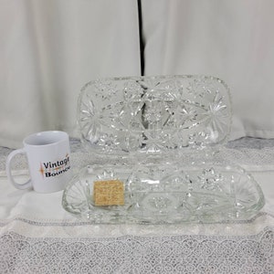 May include: Two clear glass serving dishes with a starburst pattern. The top dish is larger and has a rectangular shape. The bottom dish is smaller and has three sections.