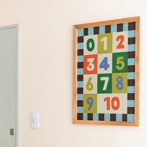 May include: A framed print featuring numbers 0-10 in a colorful grid pattern. The numbers are in various colors, including green, orange, and blue, set against a checkered background. The frame is made of light-colored wood.
