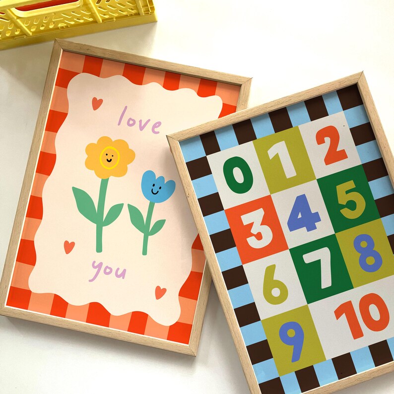 May include: Two framed art prints. One features a floral design with the words "love you" and hearts. The other displays numbers 0-10 in a grid pattern. Both have light wood frames and colorful designs.