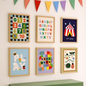 May include: A collection of six framed children's art prints with a wooden frame. The prints feature colorful illustrations of numbers, the alphabet, a circus tent, the word "PLAY", a bookworm, and other playful designs. A colorful banner hangs above.