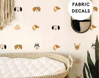 May include: A wall featuring multiple small, colorful fabric decals of various dog breeds in different poses and expressions. The decals are arranged in a repeating pattern across the surface. A white circular overlay displays the text FABRIC DECALS.